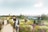 Menschen spazieren auf einem Weg durch einen blühenden Garten mit Brücke im Hintergrund.