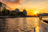 Sonnenuntergang über einem Fluss mit Gebäuden am Ufer und einem Boot im Vordergrund.