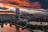 Stadtpanorama mit Hochhaus und Fluss bei Sonnenuntergang.