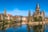 Fluss mit historischer Kirche und Gebäuden im Hintergrund, blauer Himmel.