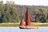 Segelboot auf einem See vor bewaldeter Kulisse.