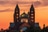 Majestätische Kathedrale bei Sonnenuntergang mit drei Türmen vor orangefarbenem Himmel.