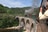 Zug fährt über eine steinerne Brücke, umgeben von Bäumen und Hügeln, mit einem fotografierenden Mann im Vordergrund.