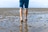 Person geht barfuss im flachen Wasser am Strand.