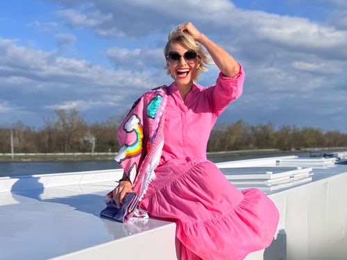 Frau in pinkem Kleid sitzt entspannt auf einer weissen Oberfläche vor blauem Himmel.
