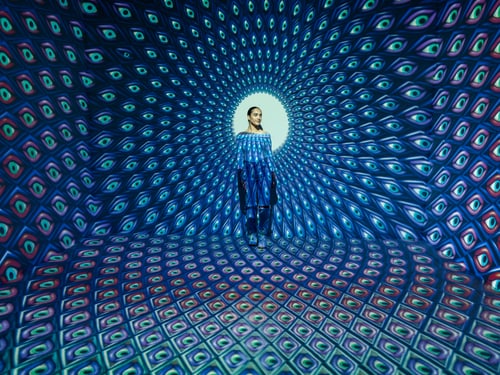 Frau steht in einem kaleidoskopischen Musterraum.