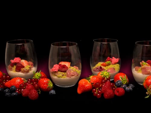 Vier Dessertgläser mit Beeren und Cremes auf schwarzem Hintergrund.