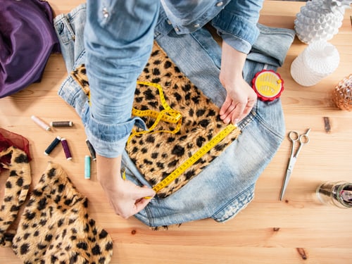 Person arbeitet mit Massband an Jeansjacke mit Leopardenstoff.