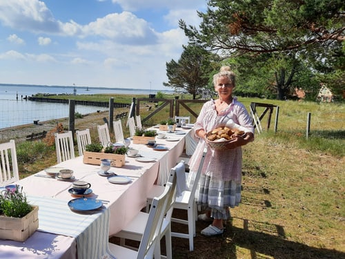 Kerstin Otto in gemustertem Kleid hält einen Korb mit Gebäck neben einem gedeckten Tisch im Freien auf der Insel Ruden.