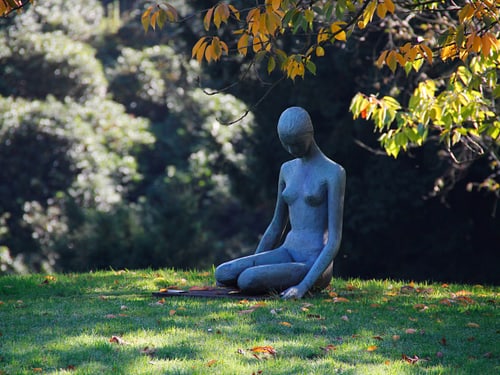 Skulptur einer sitzenden Figur auf einer Wiese im Park.