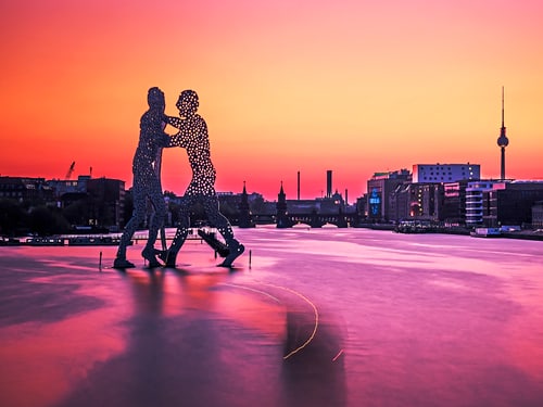 Silhouette der Molecule-Man-Skulptur auf der Spree vor Berliner Skyline im Abendrot.