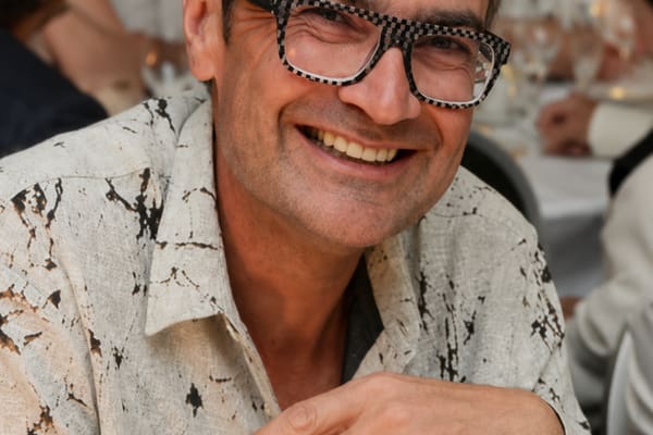 paris-die-normandie-und-das-meer-1.png Person mit Brille in weissem Hemd lächelnd bei einem formellen Essen.
