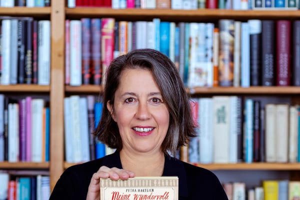 eine-donau-literatour-1.jpg Person hält ein Buch vor einem Bücherregal.