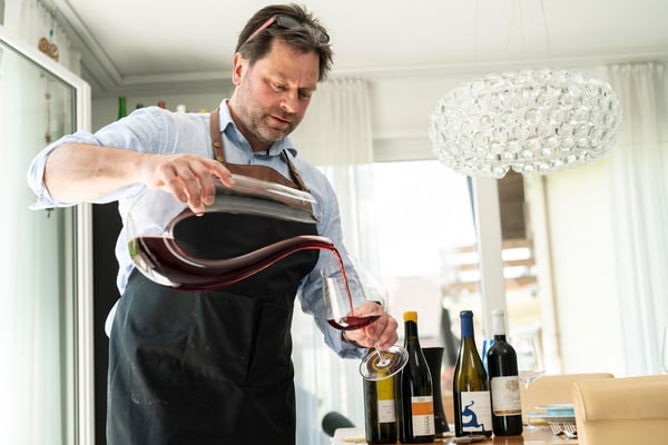 Mann in Schürze schenkt Wein aus einer Karaffe ein.