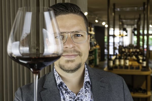 weinexperte-johannes-wagenleiter.jpg Mann mit Brille hält ein Glas Rotwein hoch.