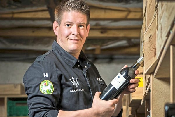 zwei-sternekoeche-viel-genuss-1.jpg Mann hält Weinflasche in einem Keller.