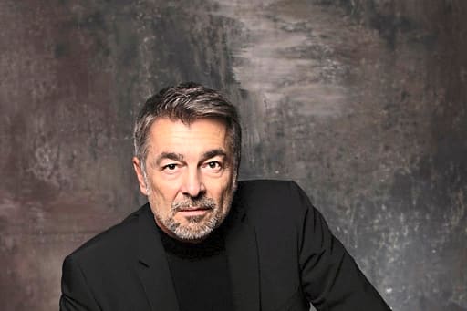 tatort-donau-mit-stefan-gubser-1.jpg Person in schwarzem Anzug sitzt vor neutralem Hintergrund.