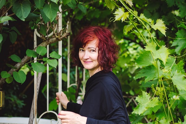 gartenparadiese-an-der-seine-1.jpg Person mit rotem Haar und Korb im Garten, umgeben von grünen Blättern.