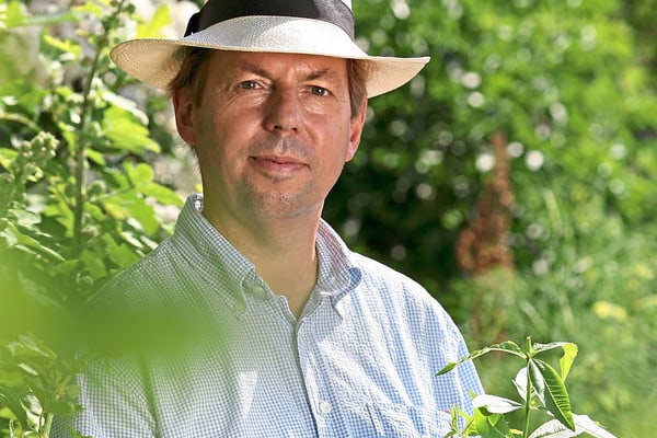 gartenkultur-an-main-und-donau-1.jpg Mann mit Hut in einem Garten stehend.