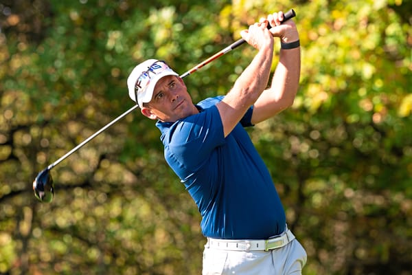 Golfer schwingt Golfschläger auf einem grünen Platz.