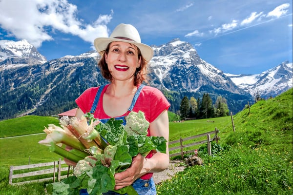 suedfrankreichs-gruene-oasen-1.jpg Person in rotem T-Shirt mit Hut hält Gemüse in einer Berglandschaft.