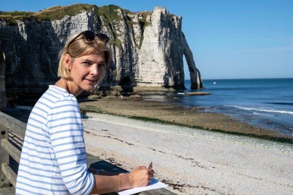 Frau am Strand mit Notizblock, Klippe im Hintergrund.