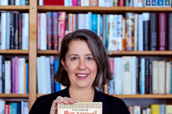 Person hält ein Buch vor einem Bücherregal.