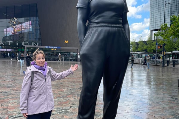 Person steht neben grosser Statue auf Platz vor modernem Gebäude.