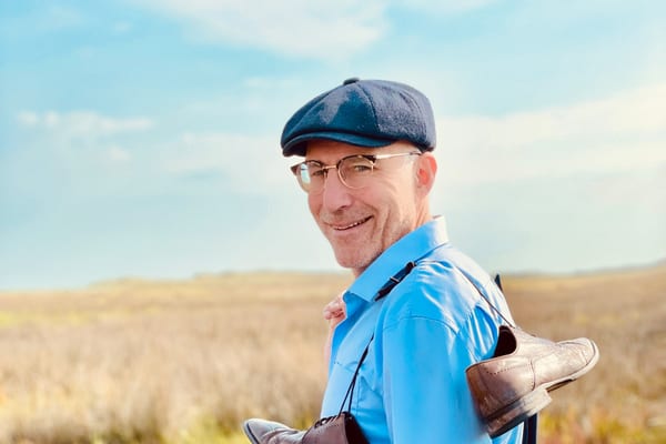 franken-und-die-oberpfalz-sommertage-zum-geniessen-1.jpg Person im blauen Hemd und Mütze steht auf einem Feld mit trockenen Gräsern.