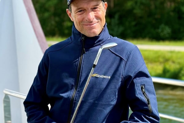 die-gruensten-seiten-der-donau-1.jpg Person in blauer Jacke und Mütze steht mit einem Golfschläger auf einem Boot.