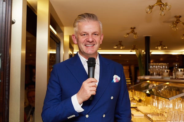 Mann in blauem Anzug mit Mikrofon in einem Restaurant.
