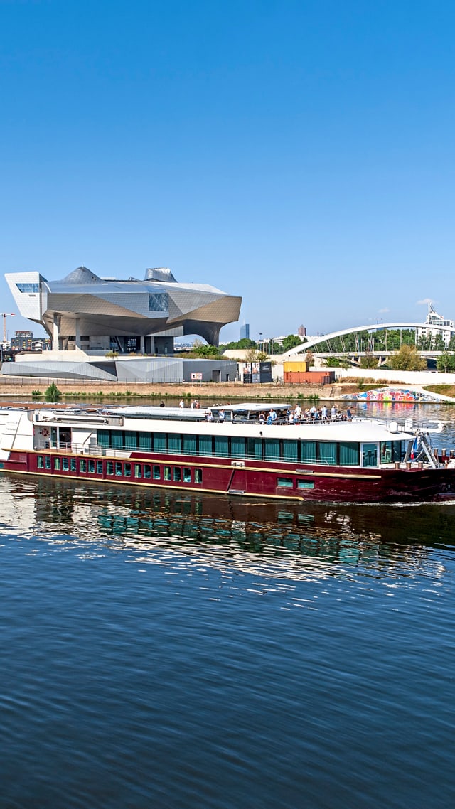excellence-rhone.jpg Schiff auf einem Fluss vor einem modernen Gebäude.