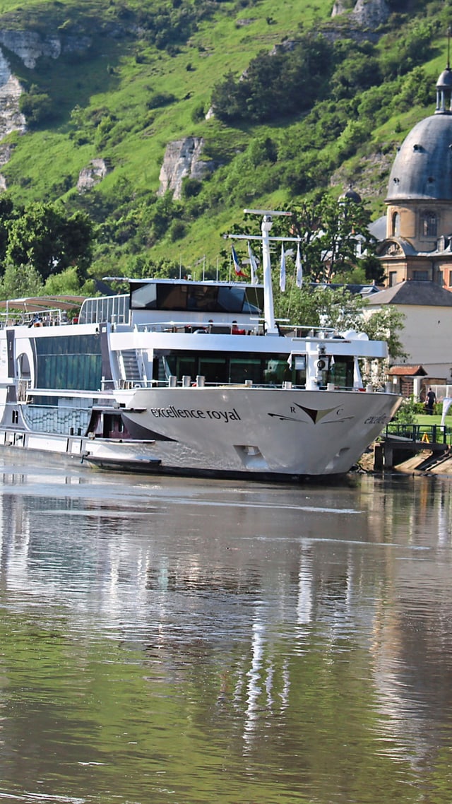 excellence-royal.jpg Flusskreuzfahrtschiff auf der Elbe vor malerischer Hügellandschaft.