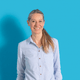 Lächelnde Person mit hellblauer Bluse vor blauem Hintergrund.