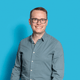 Person mit Brille und Hemd vor blauem Hintergrund.