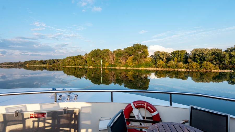 Blick von einem Boot auf ruhigen Fluss und bewaldetes Ufer.