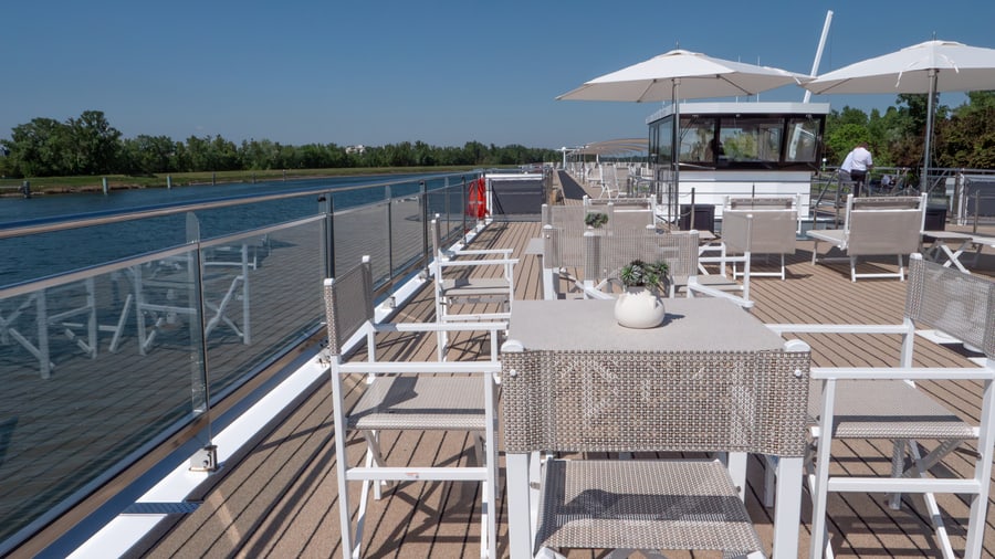Sonnendeck eines Schiffes mit Tischen und Stühlen am Fluss.