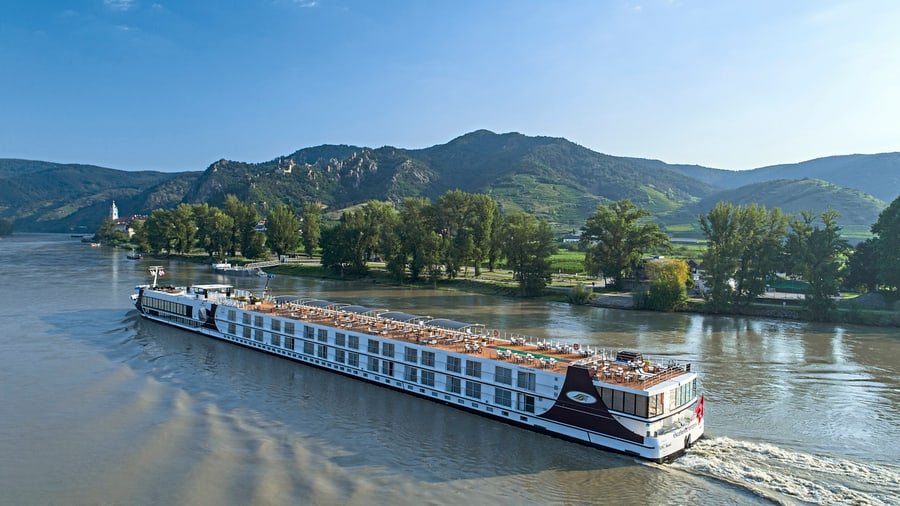 Kreuzfahrtschiff auf Fluss vor bewaldeten Hügeln.