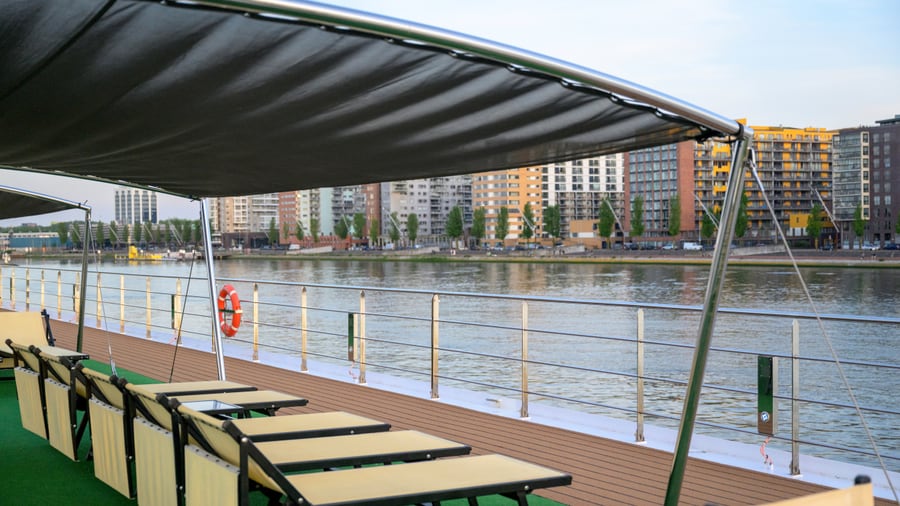 Deck eines Schiffes mit Liegestühlen am Flussufer.