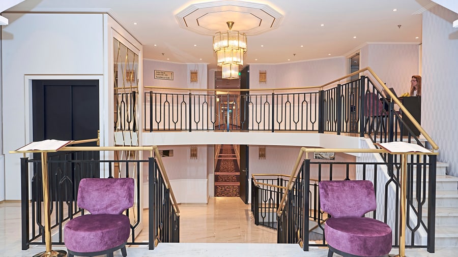 Elegantes Treppenhaus mit lila Sessel, goldenen Geländern und Kronleuchter.