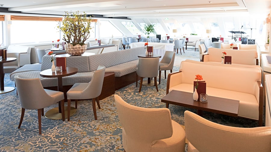 Elegante Lounge mit Tischen und Sesseln auf einem Kreuzfahrtschiff.
