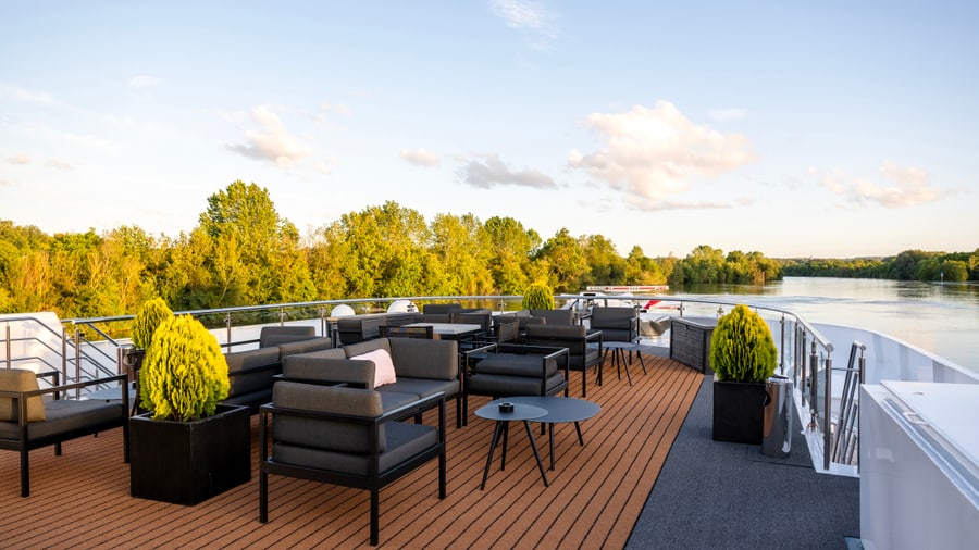 Terrasse eines Schiffs mit Sitzmöbeln auf einem Fluss, umgeben von Bäumen.