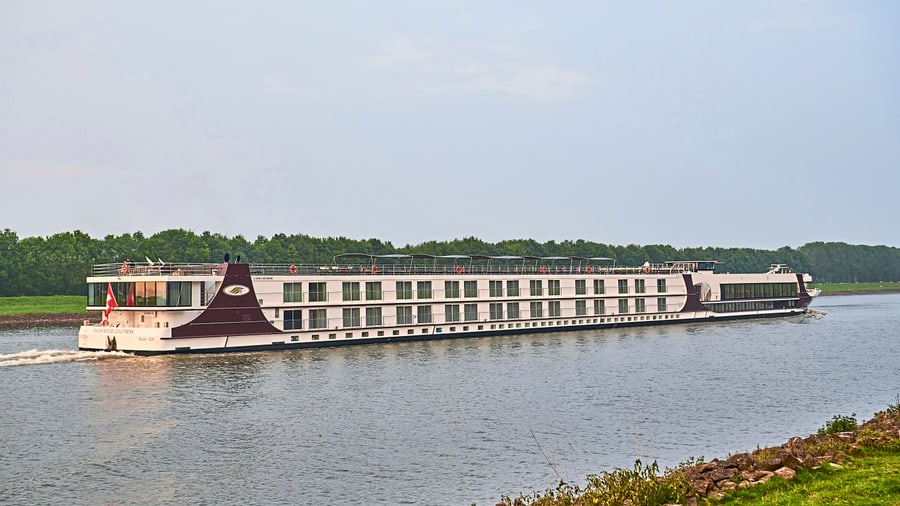 Langes Kreuzfahrtschiff auf einem Fluss mit grünem Ufer.