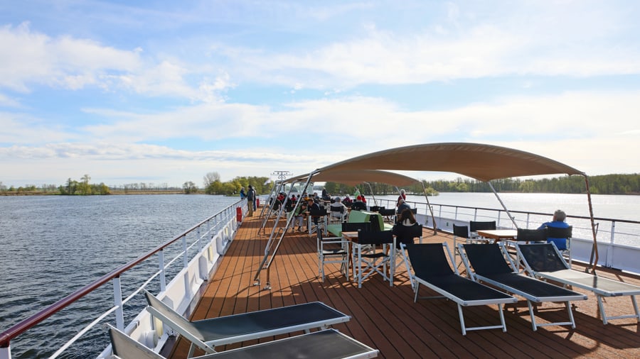 Menschen auf dem Deck eines Schiffes mit Liegestühlen und Sonnendach.