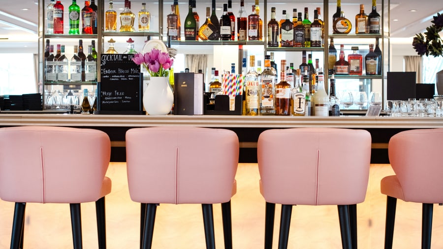 Moderne Bar mit rosa Hockern und Flaschenregal.