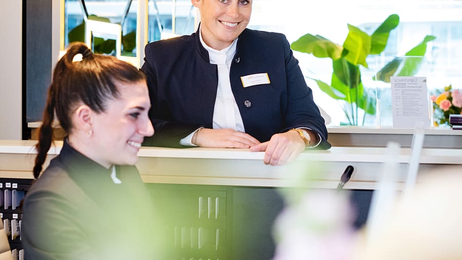 Zwei lächelnde Frauen in Büro-Outfit an einem Tresen.