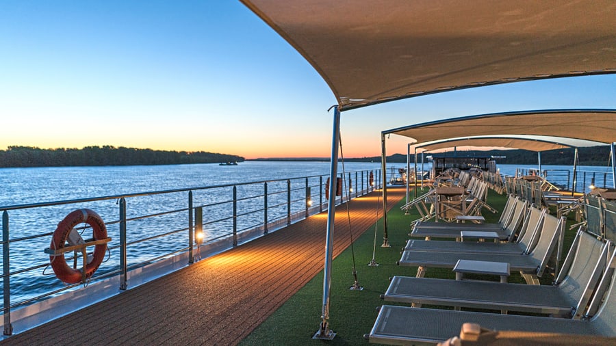 Deck eines Flusskreuzfahrtschiffs bei Sonnenaufgang, mit Liegestühlen und Wasserblick.