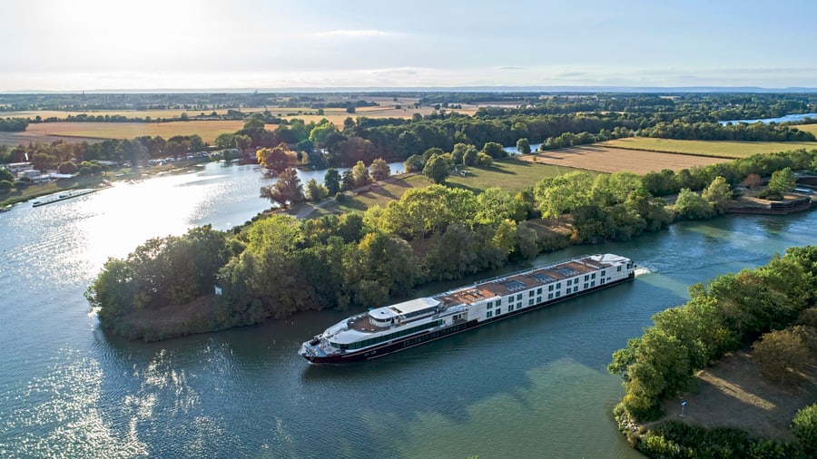 Flusskreuzfahrtschiff fährt auf einem Fluss durch eine ländliche Landschaft.