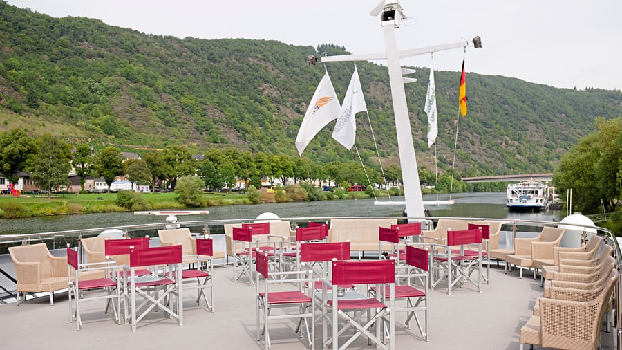 Deck eines Flusskreuzfahrtschiffs mit leeren Stühlen und Flusslandschaft.