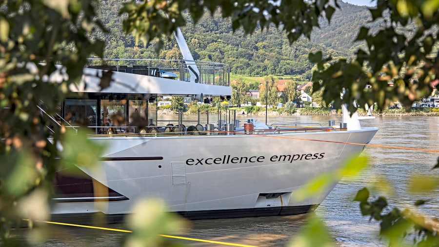 Kreuzfahrtschiff Excellence Empress auf einem Fluss, umgeben von Bäumen.